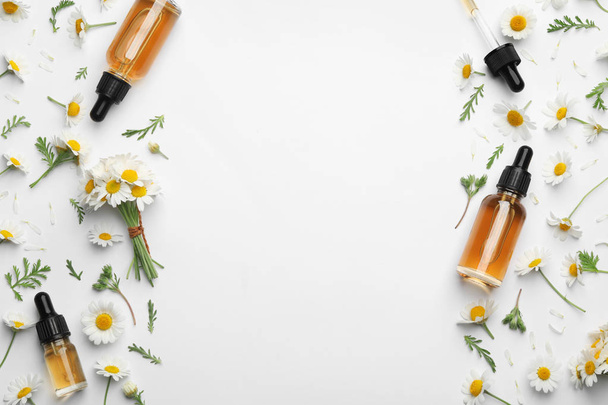 Chamomile flowers and cosmetic bottles of essential oil on white background, top view. Space for text - 写真・画像
