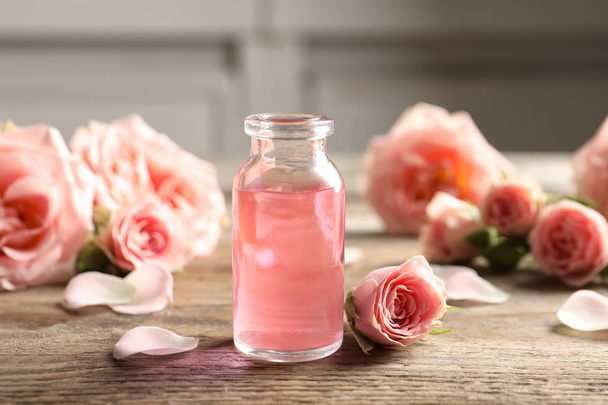 Bottle of rose essential oil and flowers on wooden table - Valokuva, kuva