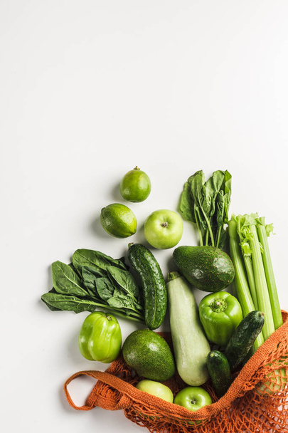 Green vegetables and fruits in orange string bag - Фото, изображение