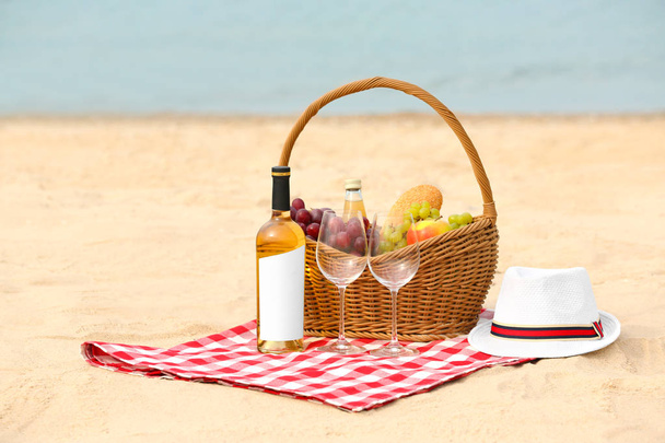 Wicker basket with food and wine on blanket near sea, space for text. Summer picnic - Foto, Bild