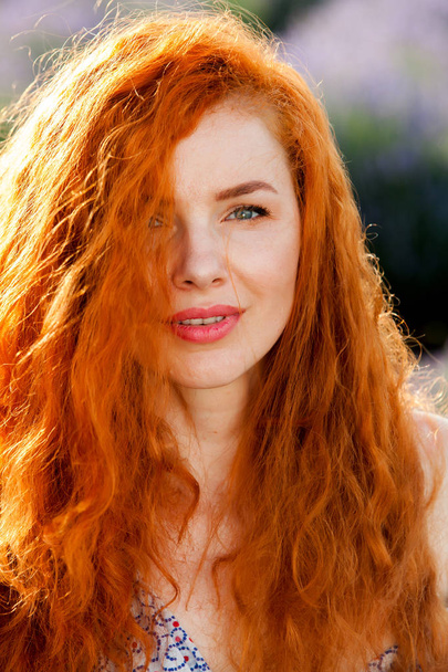 Portrait d'été d'une belle fille aux longs cheveux roux bouclés. femme aux cheveux longs. Fille européenne dans le champ de lavande
. - Photo, image