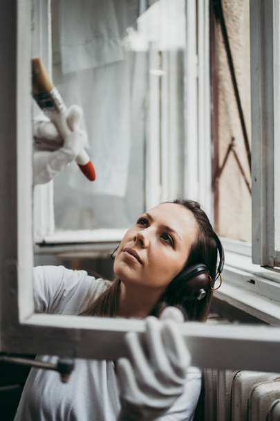 Krásná a pilný středního věku šikovná žena renovuje svůj starý domov nebo byt. Drží profesionální štětec a maluje okna. Udělej si to sám.. - Fotografie, Obrázek