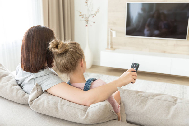 Mother and daughter sitting on sofa watching tv - Photo, Image
