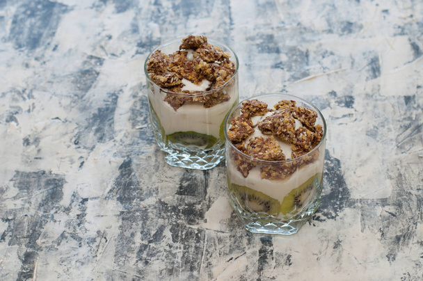 Granola, kiivi, banaani ja kreikkalainen jogurtti lasikupeissa harmaalla betonilla
 - Valokuva, kuva