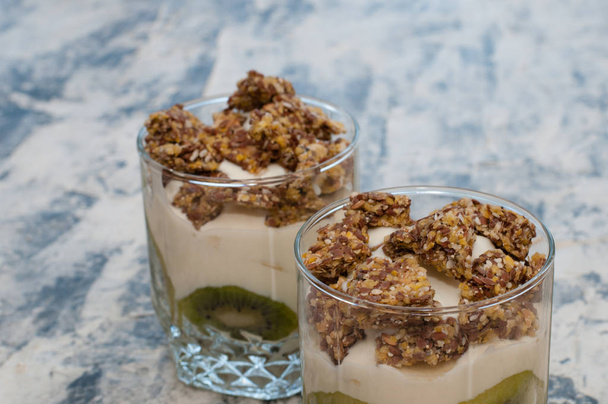 Granola, kiwi, banana e iogurte grego em duas xícaras de vidro em concreto cinza
 - Foto, Imagem