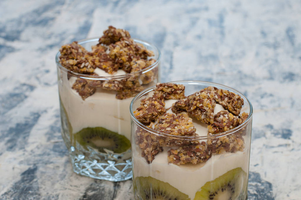 Granola, kiwi, banana e iogurte grego em duas xícaras de vidro em concreto cinza
 - Foto, Imagem