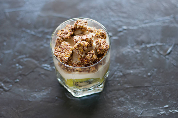 ギリシャヨーグルト グラノーラ バナナとキウイ暗い背景にガラスビーカーのデザート。コンセプトボディと健康食品 - 写真・画像