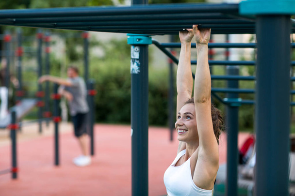 Young woman is training on the outdoor playground and pulls up on the horizontal bar. Crossfit and fitness workout outdoors. - Foto, Imagen