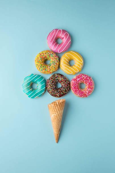 Ice-cream made of colorful donuts and waffle cone on light blue background.  - Foto, afbeelding