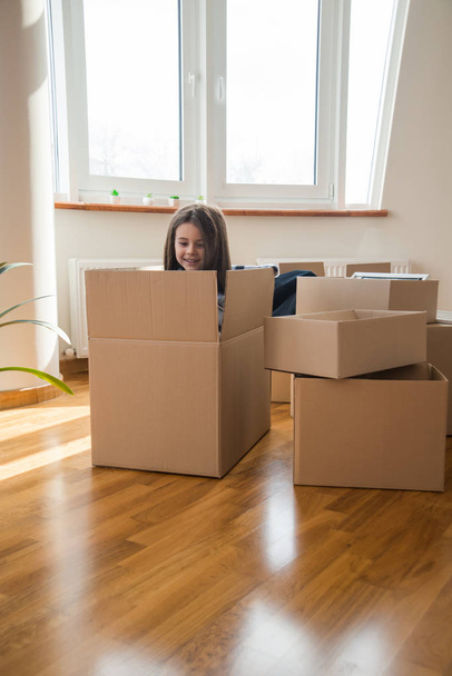 Boldog gyerek lánya a dobozban izgatott költözés vagy áthelyezés, vidám lány játszik kicsomagolás új otthon szórakozás - Fotó, kép