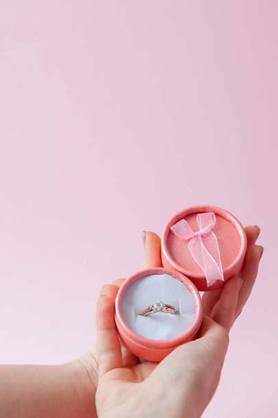 Woman opens a gift box with jewellery. Wedding ring in a box in the hands of women on a pink background - Foto, Bild