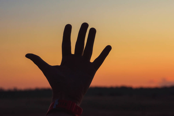 Hand Guy op de achtergrond van een oranje zonsondergang. Openluchtrecreatie in Kazachstan. Oranje zonsondergang in de lucht. - Foto, afbeelding