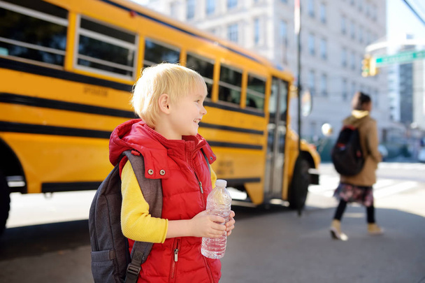 Pupil with schoolbag and bottle of water with yellow school bus on background. - Photo, Image