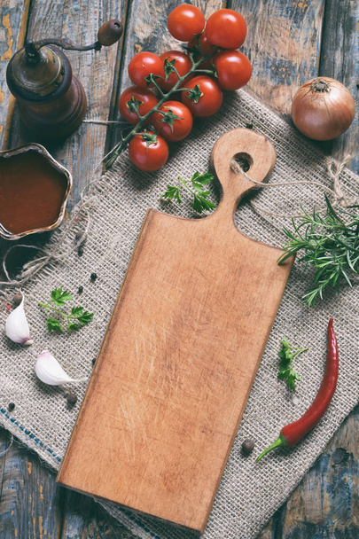 Rustic composition with wooden board, pepper mill, tomato souce, fresh herbs, vegetables and spices. Country style. Baking or cooking background. Copy space for text, menu, recipes. - Photo, Image