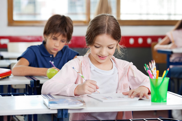 Schoolgirl Smiling While Drawing In Classroom - Foto, afbeelding
