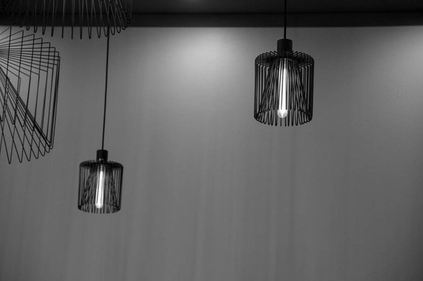 Two metal wire chandeliers are hanging on empty wall background. Modern lampshade. Lamps with long light bulbs inside. Geometric line shapes. Minimal backdrop. Interior decorations. Black and white  - Photo, Image