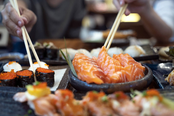 Ασιάτης/ισσα κυρία τρώνε ένα ψάρι σολομού σασίμι και σούσι σε Ιαπωνικά Resta - Φωτογραφία, εικόνα
