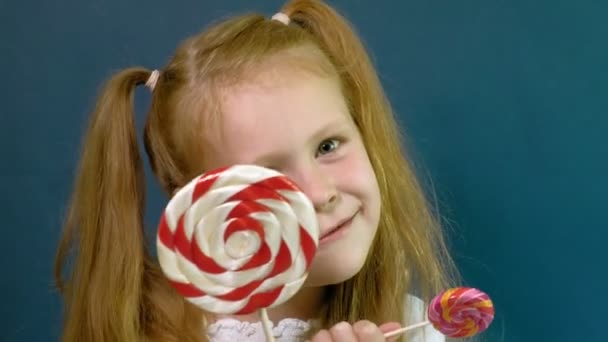 Little girl with a lollipop on a blue background. Close up portrait - Footage, Video