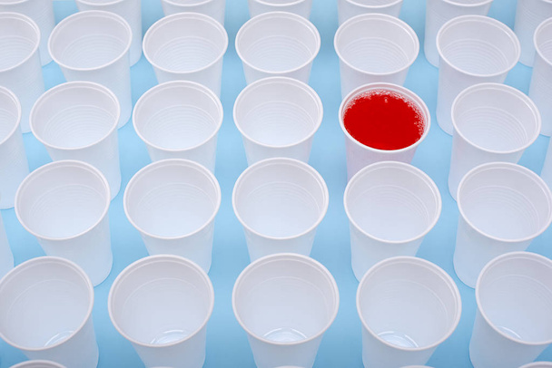 Kertakäyttöiset muoviset valkoiset tyhjät kupit ja yksi lasi täynnä punaista limonadia
 - Valokuva, kuva