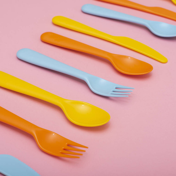 Vajilla colorida: cuchara, cuchillo, tenedor en gama sobre fondo rosa
. - Foto, Imagen