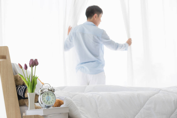 Asian man parts the curtain in bedroom - Foto, immagini