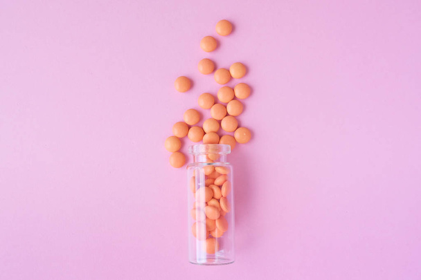 Orange tablets from glass bottle on pink background. copyspace for text. Epidemic, painkillers, healthcare, treatment pills and drug abuse concept. flat lay. top view - Foto, afbeelding