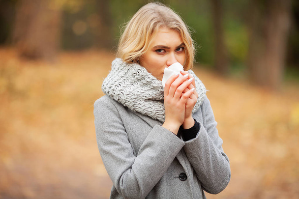Chica estornudando en tejido. Una joven sonándose la nariz en el parque. Mujer retrato al aire libre estornudos porque el frío y la gripe
 - Foto, imagen