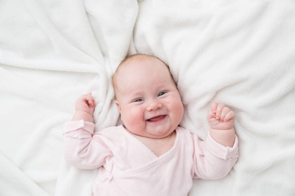 Новорожденная девочка позировала на спине, на одеяле из меха, улыбаясь, глядя в камеру
 - Фото, изображение