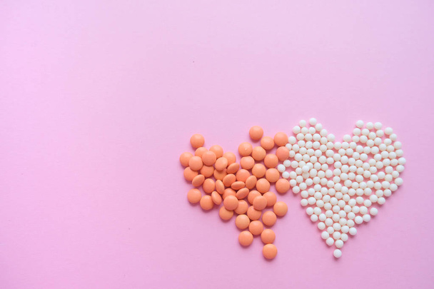 Two hearts made of homeopathic globules and orange pills on pink background. Homeopathy medicine, healtcare, Epidemic, painkillers, drug and pills concept. Flatlay. Top view. copyspace for text - Фото, зображення