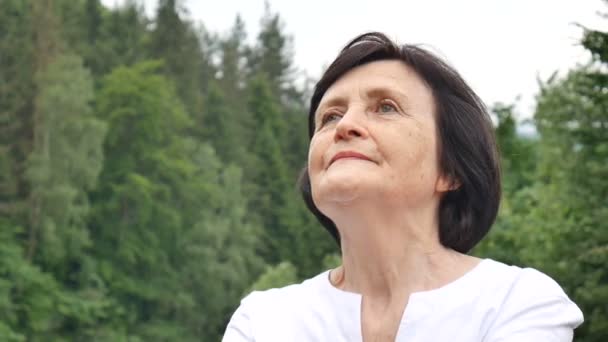 Starsza kobieta robi ćwiczenia rozciągające dla górnych ramion poza krajobraz lasu i gór - Materiał filmowy, wideo