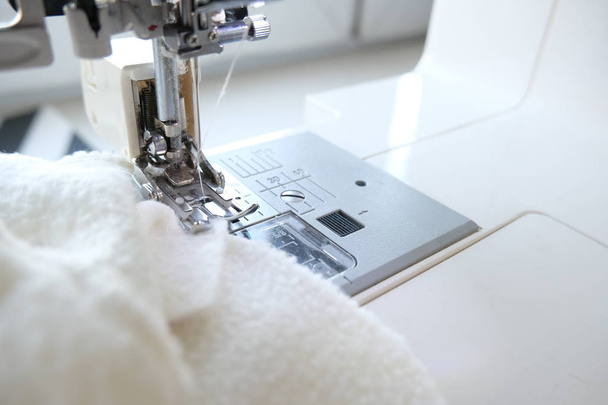 Close up sewing machine with white fabric textile at workplace. Sew process. - needlework, craft, sewing and tailoring concept - 写真・画像