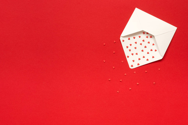 Red Sweets sprinkles candy hearts fly out of white paper envelope on red background. Top view Copy space for text. Concept Valentines day and Valentine card. Gift, message with love - Photo, Image