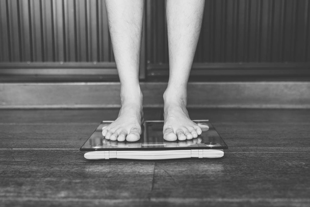 Man op gewicht schaal op vloer achtergrond, dieet concept. - Foto, afbeelding