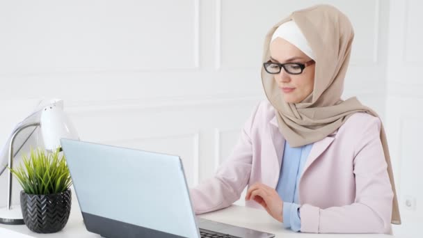 Tired muslim woman works and types on laptop, puts off her glasses and rubs her eyes. - Felvétel, videó