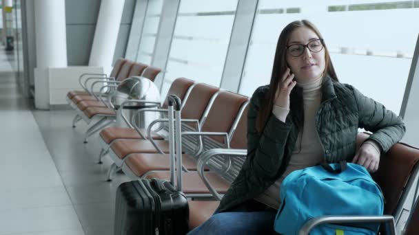 Счастливая женщина разговаривает по мобильному телефону ждет свой рейс в аэропорту
. - Кадры, видео