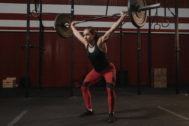 Young crossfit female athlete lifting heavy barbell overhead at  - Fotoğraf, Görsel