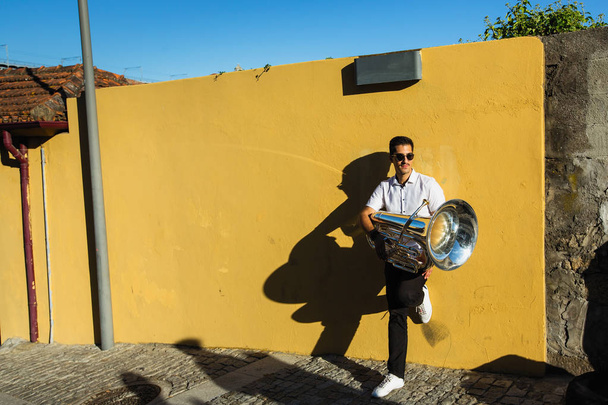 Músico con una tuba está en la calle cerca de la pared amarilla
. - Foto, Imagen