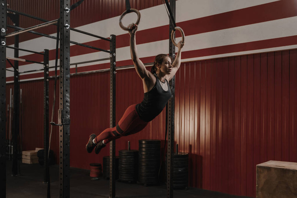 Young crossfit woman swinging on gymnastic rings. - Fotoğraf, Görsel