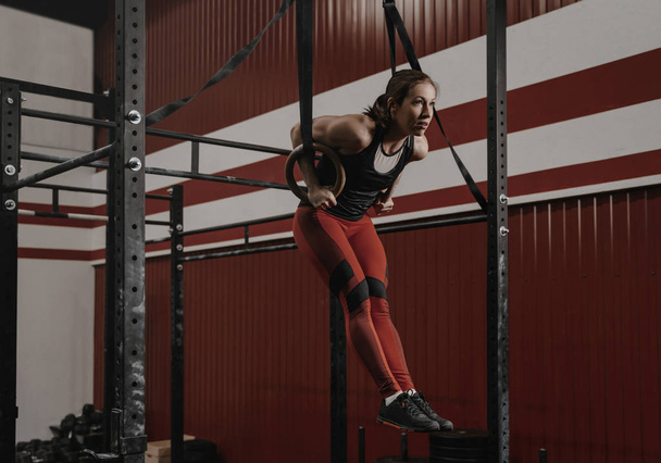 Jonge crossfit vrouw doet muscle-ups op gymnastische ringen bij de  - Foto, afbeelding