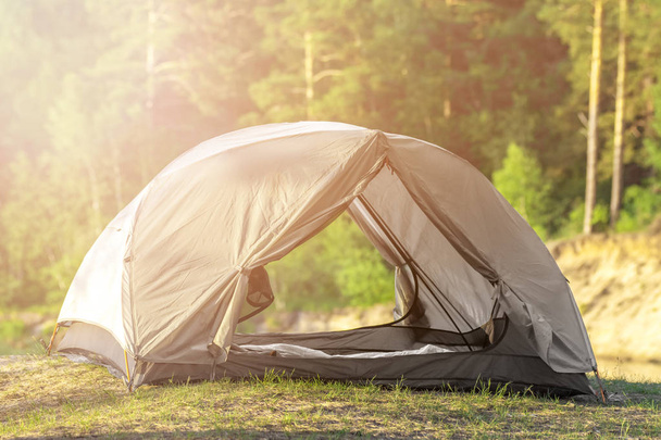 日光を浴びて野生の自然の森の近くの緑の草の上に建てられた灰色のキャンプテント - 写真・画像