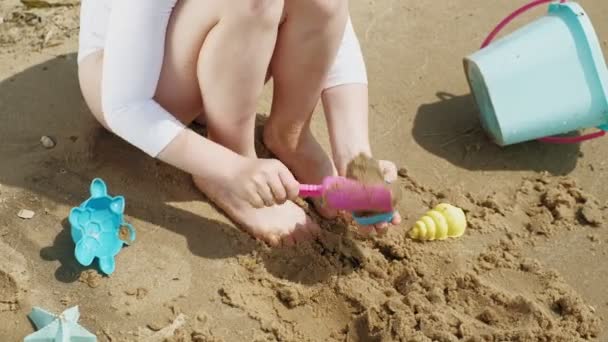 Girl child plays with sand on the beach using molds figurines. Sunny summer day. vacation - Footage, Video