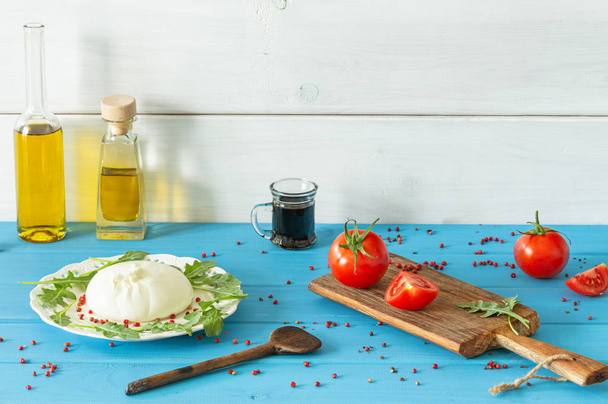 Μπουρράτα, ιταλικό τυρί με ντομάτες, μπαχαρικά, μπαγκούλα και ελαιόλαδο και ξύδι βαλσάμικο/μπλε ξύλινο τραπέζι/θέση για κείμενο - Φωτογραφία, εικόνα