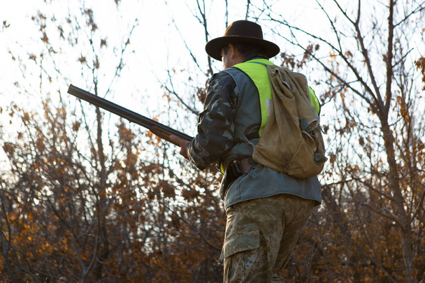 Jagdzeit, Herbstsaison geöffnet. Ein Jäger mit einem Gewehr in der Hand in Jagdkleidung im herbstlichen Wald auf der Suche nach einer Trophäe. - Foto, Bild