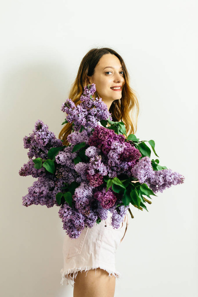白い背景にライラックの紫色の花束を持つ魅力的な女の子 - 写真・画像
