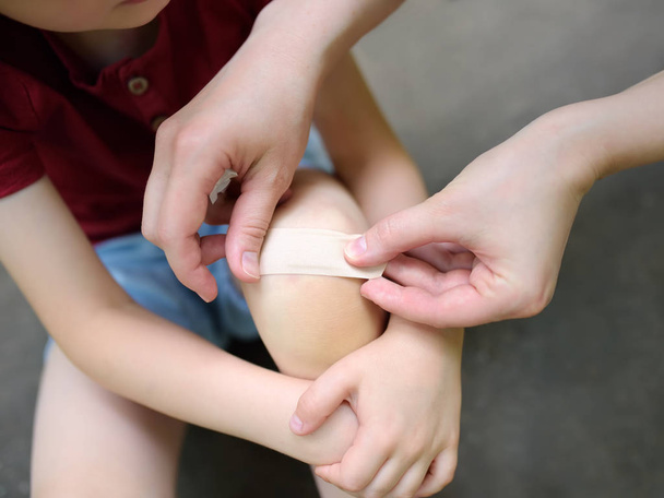 Mother hands applying antibacterial medical adhesive plaster on child's knee after falling down. - 写真・画像