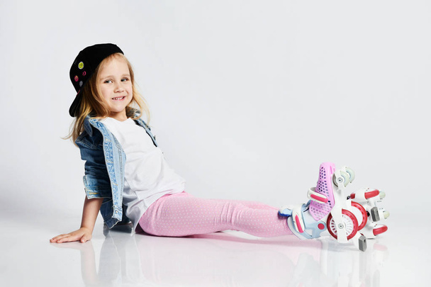 girl sits on the rollers in a blue denim and cap and smiles. Summer sports for children. - Foto, Imagen