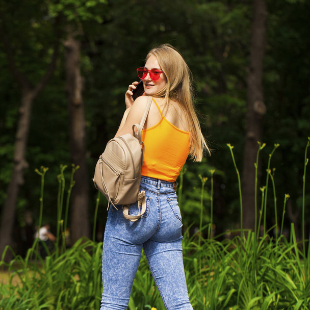 Fiatal gyönyörű nő mobiltelefonnal sétál a nyári parkban - Fotó, kép