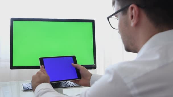 Engineer, Constructor, Designer in Glasses Working on a Personal Computer with a Green Screen on Monitor which has Chroma Key Great for Mockup Template. Male Using Smartphone or Tablet with Blue Screen and Creating, Designing using CAD Software - Footage, Video