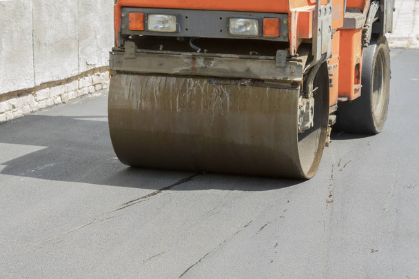 Roboty drogowe. Układanie asfaltu. Przednia część asfaltowego lodowiska jest przedstawiona. naprawy dróg. zagęszczenie chodnika w budownictwie drogowym. ciężka praca - Zdjęcie, obraz