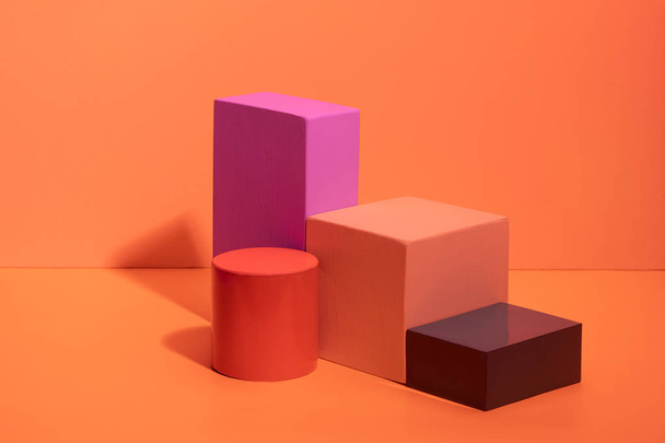 Geometric shapes in different colors on orange background. Three-dimensional solid figures on colored paper. - Foto, Imagen